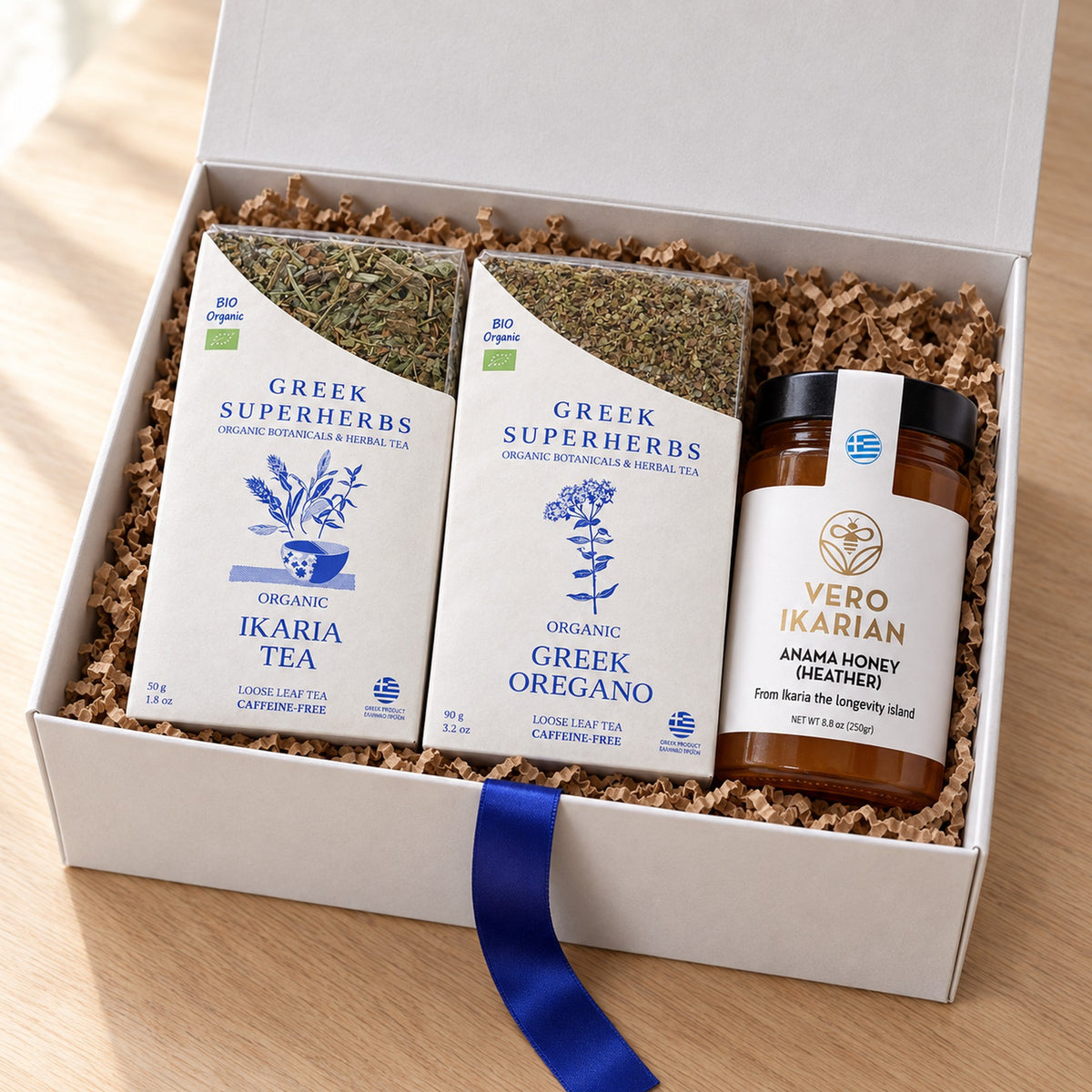 Ikaria Longevity Ritual Gift Set — Ikaria tea, Greek oregano and heather honey in an open white gift box with kraft crinkle paper and blue ribbon