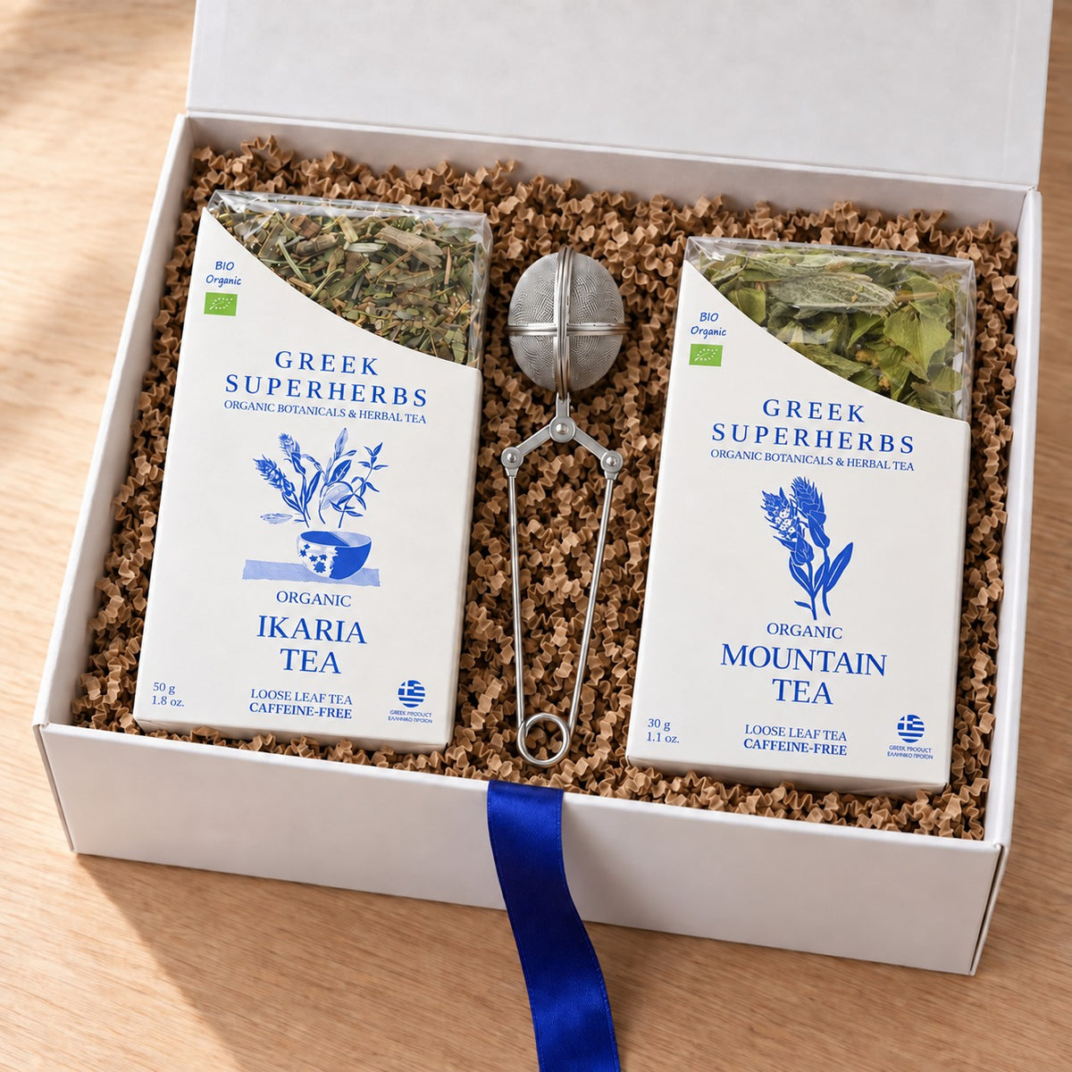 Ikaria & Olympus Duo Gift Set — Ikaria Blue Zone Tea, Organic Mountain Tea and snap tea-ball infuser in a white gift box with kraft crinkle paper
