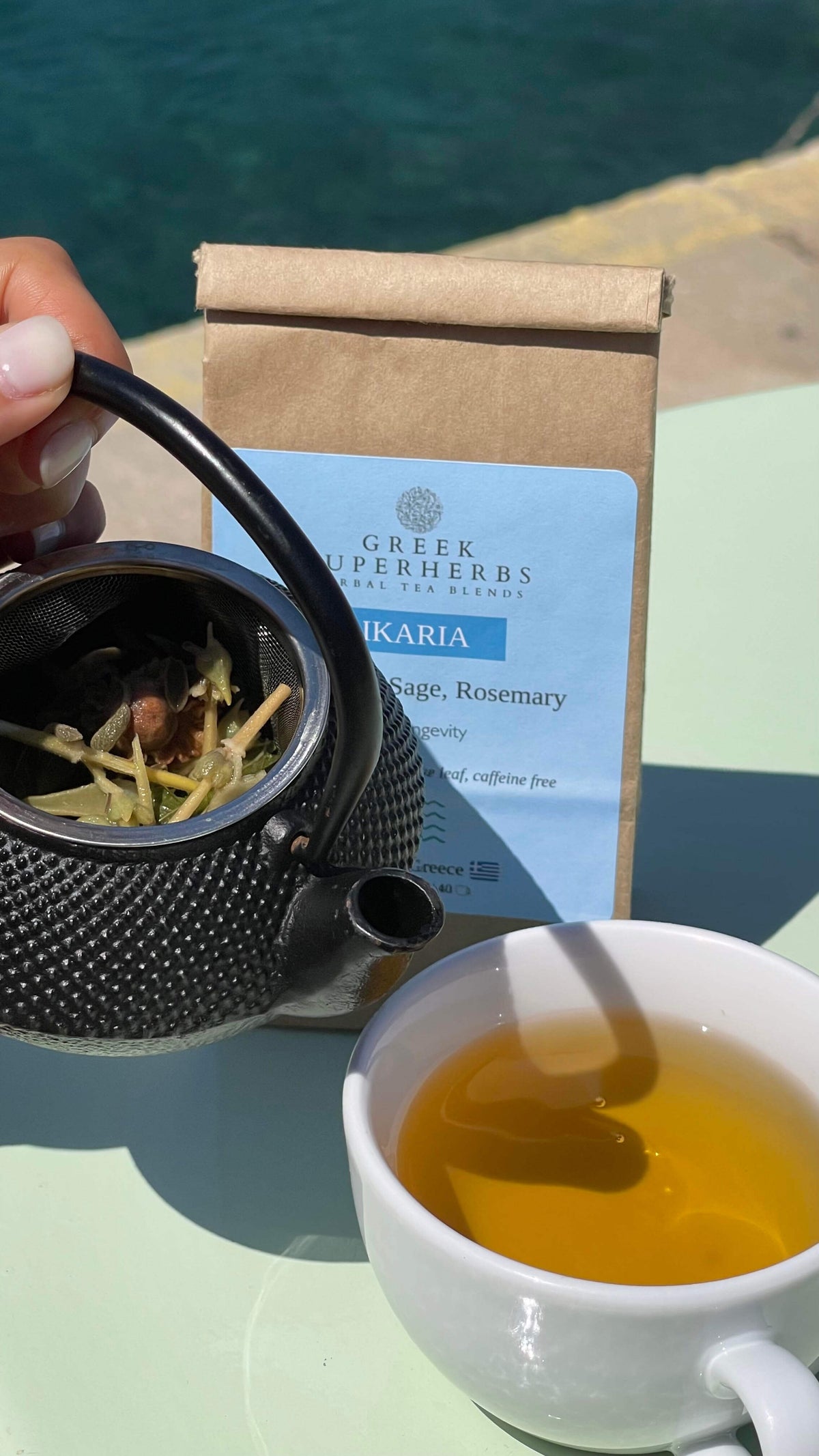 A cast-iron teapot and glass of Ikaria Blue Zone Tea by the Aegean sea