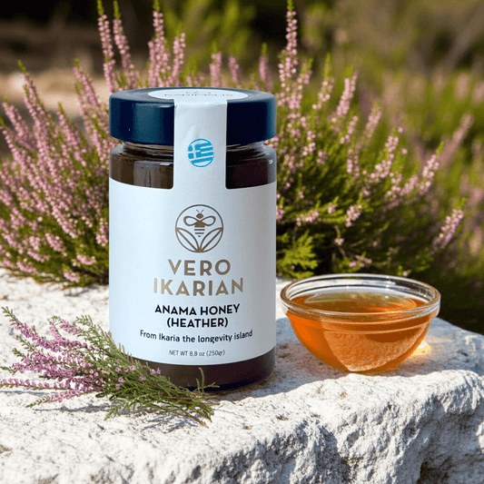 Jar of Ikarian Anama Honey with a small bowl of honey on a stone surface with heather in the background.