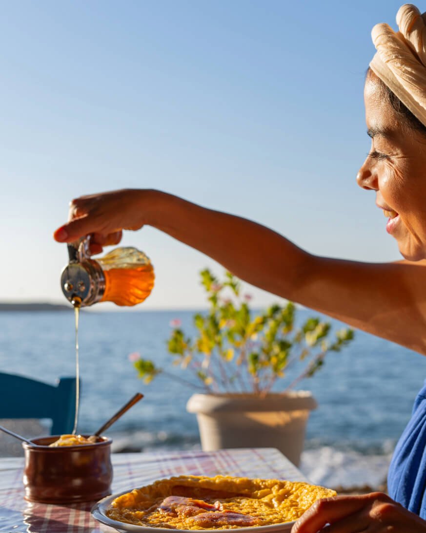 Pouring raw Ikaria thyme honey from a glass jar by the sea
