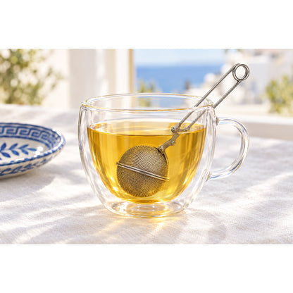 Tea ball infuser steeping golden herbal tea in a glass cup